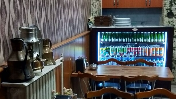 Zona pranzo con tavolo in legno e sedie metalliche, frigorifero fornito di bevande e oggetti decorativi appesi al muro.
