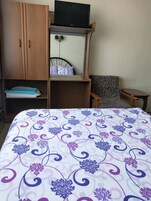 Un dormitorio con una cama, un televisor en un estante, una silla y una mesita.