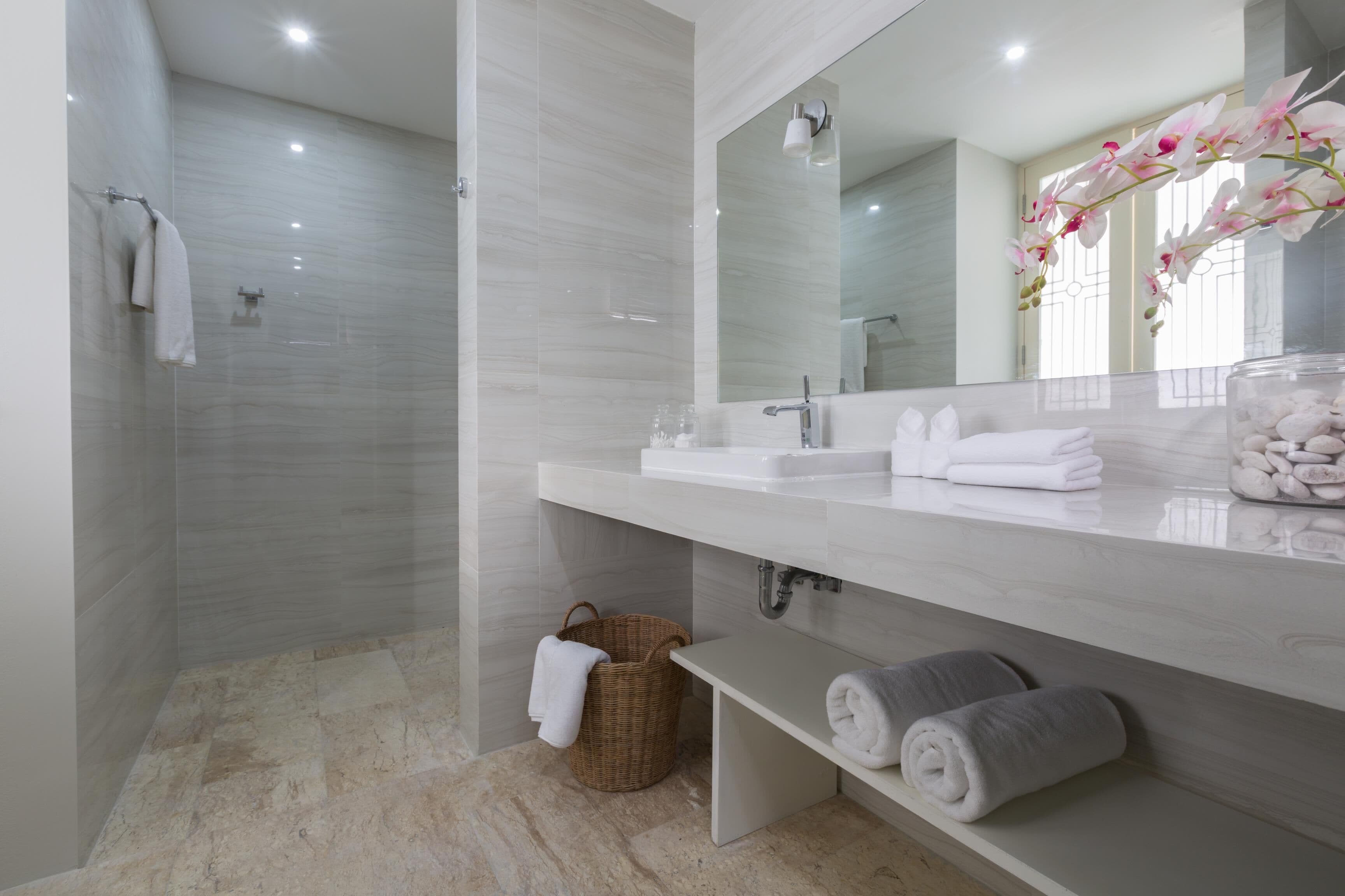 A modern bathroom with a glass shower enclosure, a large mirror, and a marble countertop with towels.