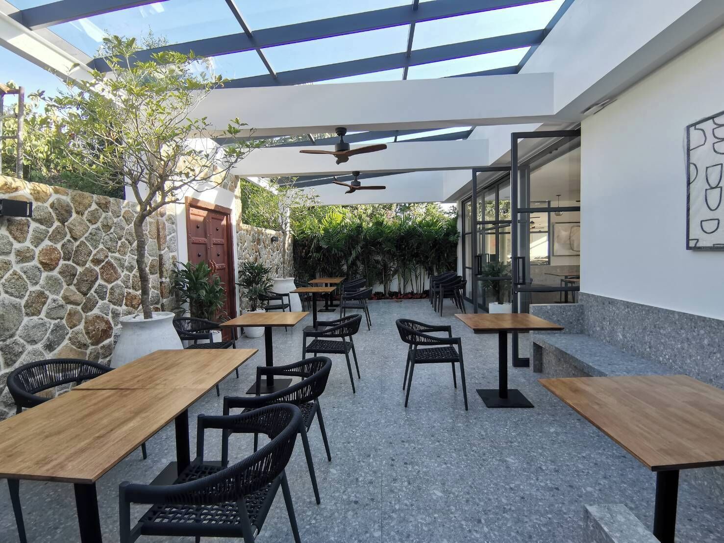 An outdoor patio area with stone walls, wooden tables, and black chairs.
