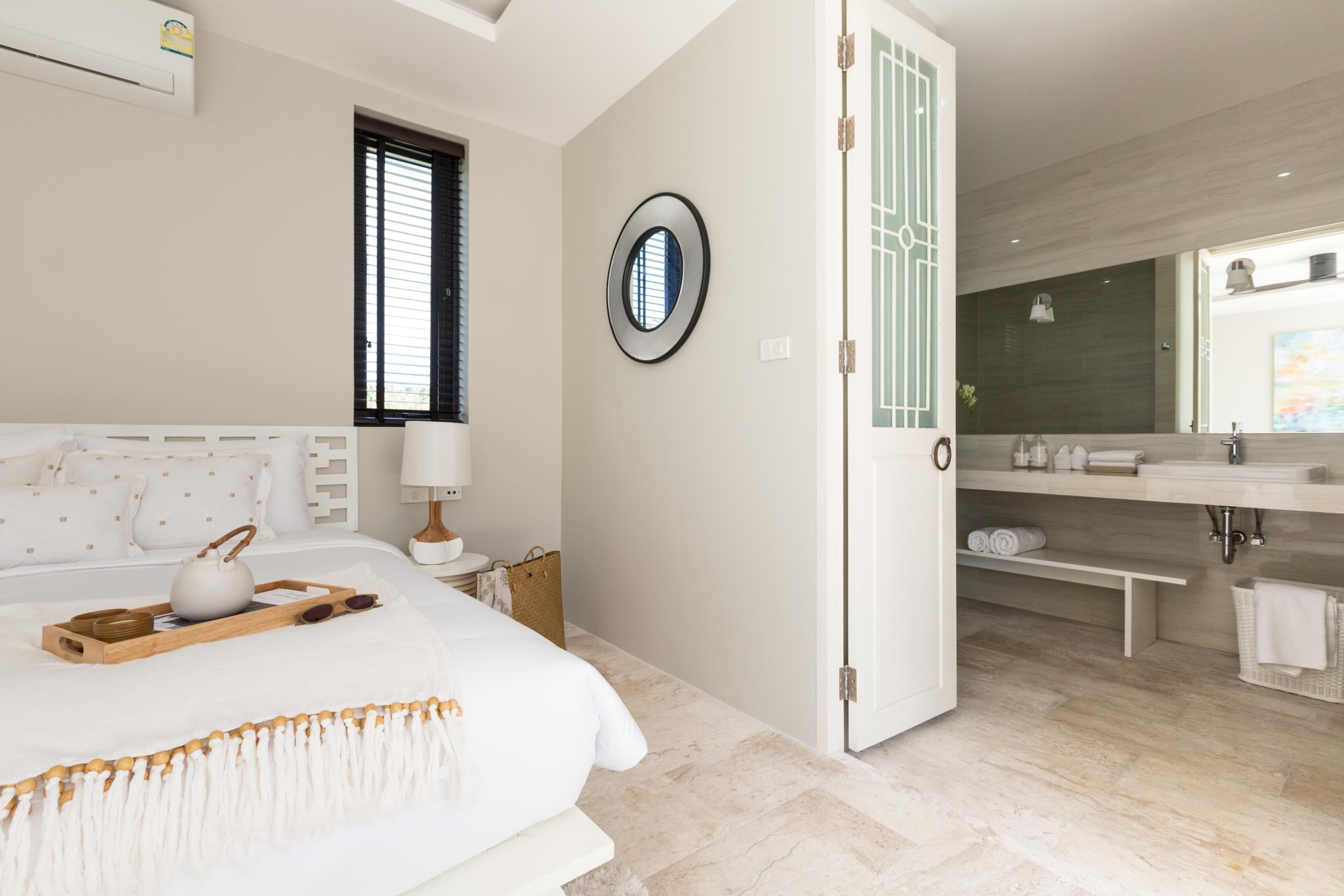 A modern bedroom with a bed, bedside table, and a bathroom with a sink and mirror.