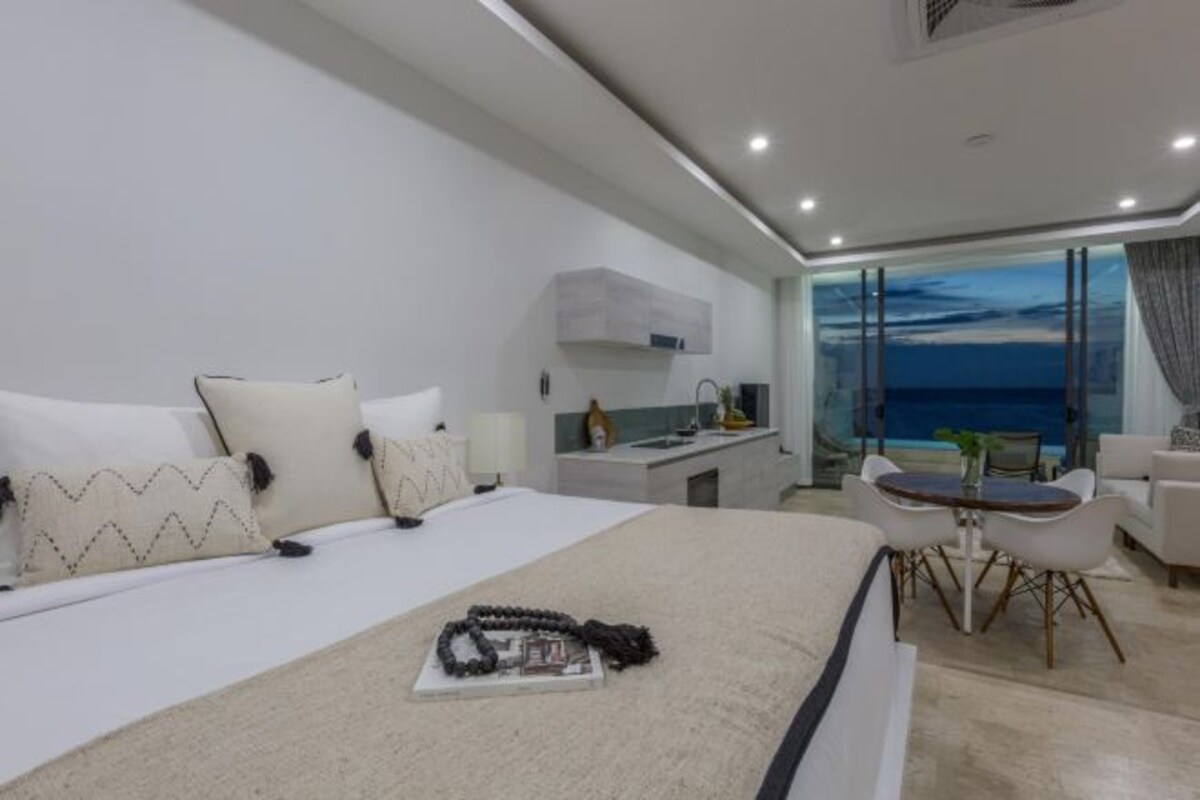 Ett modernt hotellrum med en stor säng, ett skrivbord och en matplats med utsikt över havet.