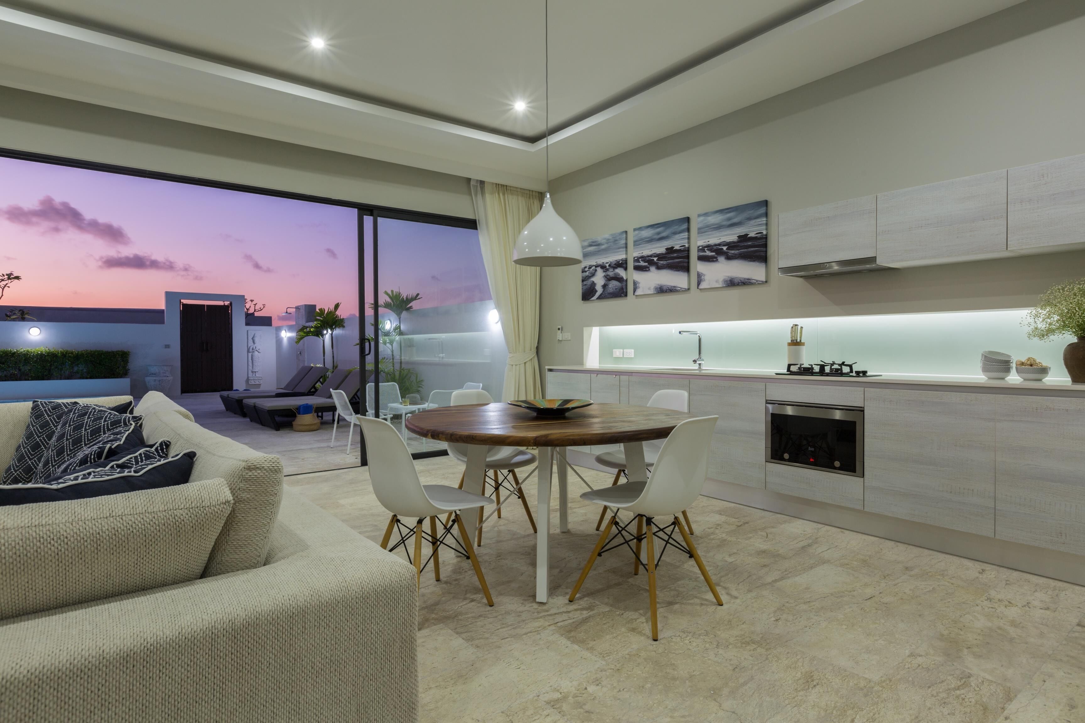 A modern kitchen with a dining area, large windows, and a view of the sunset.