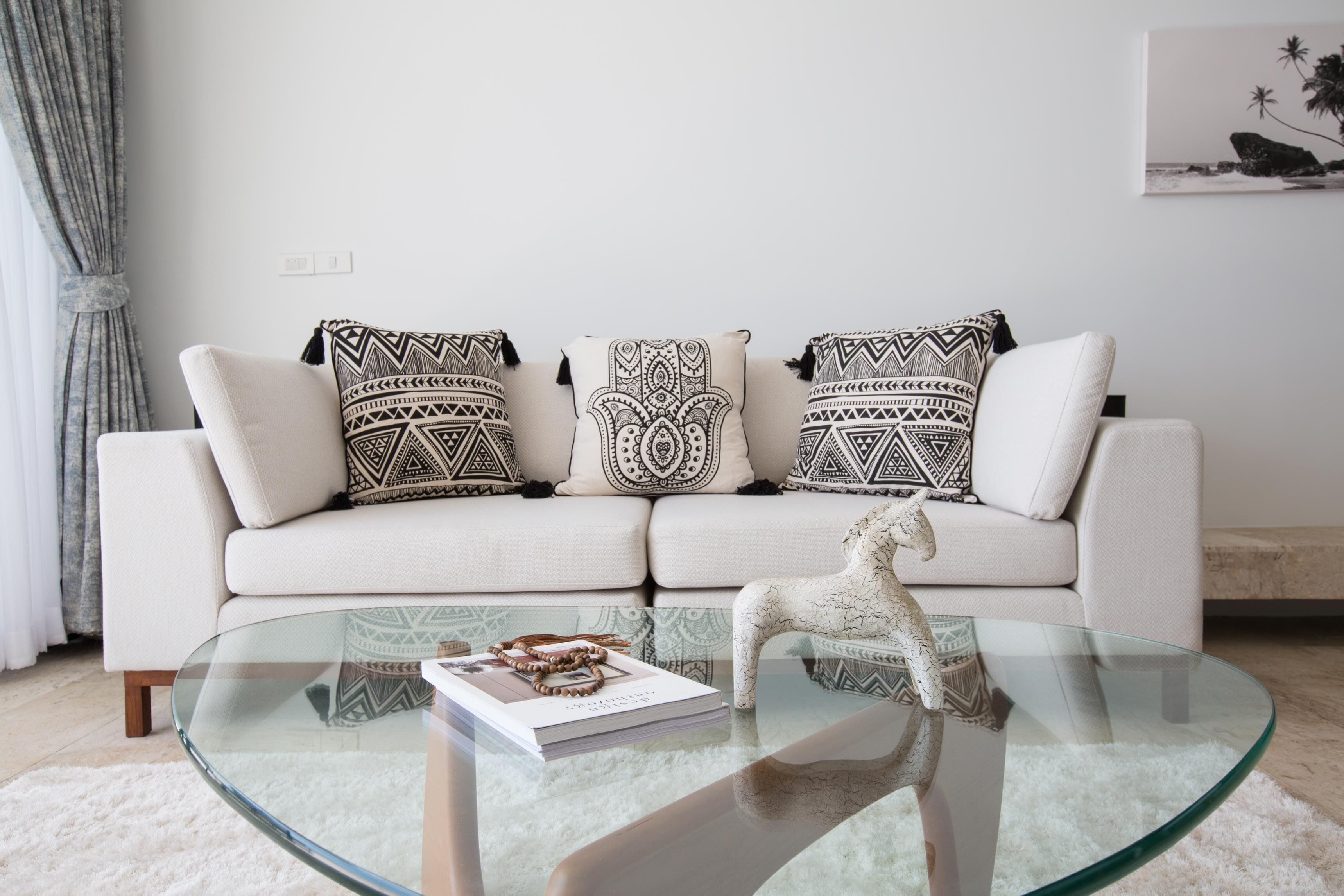 A modern living room with a white sofa, patterned cushions, a glass coffee table, and a decorative horse statue.