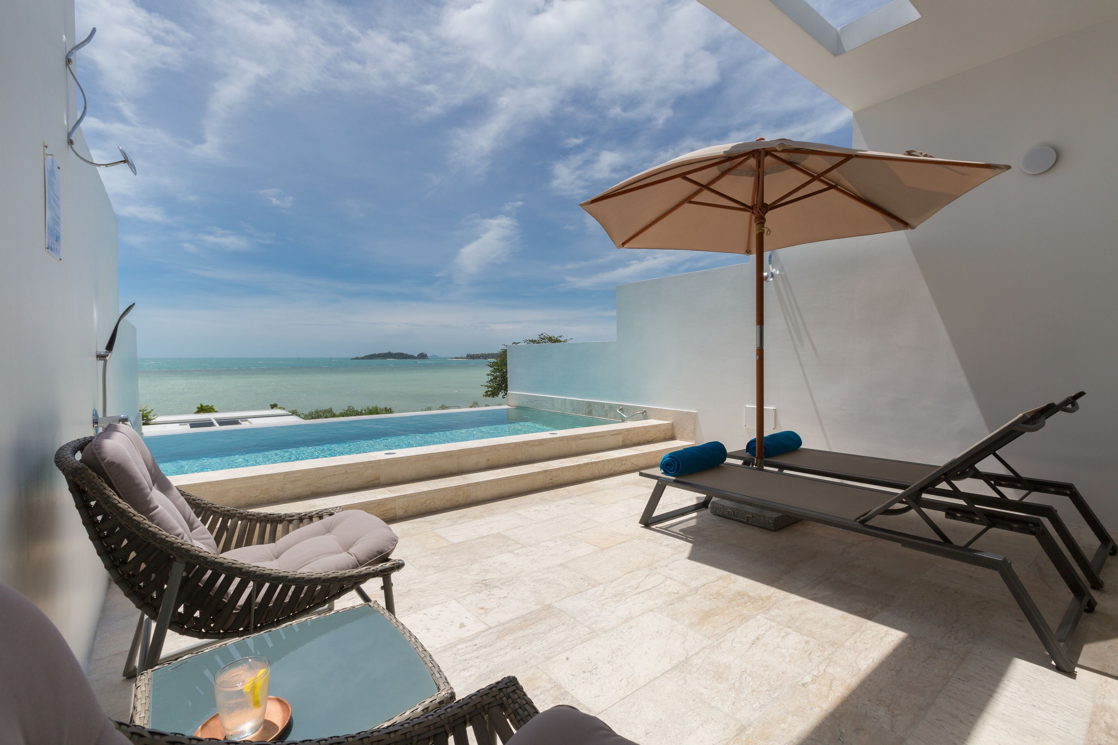 A balcony with a pool, lounge chairs, and a table with a drink.