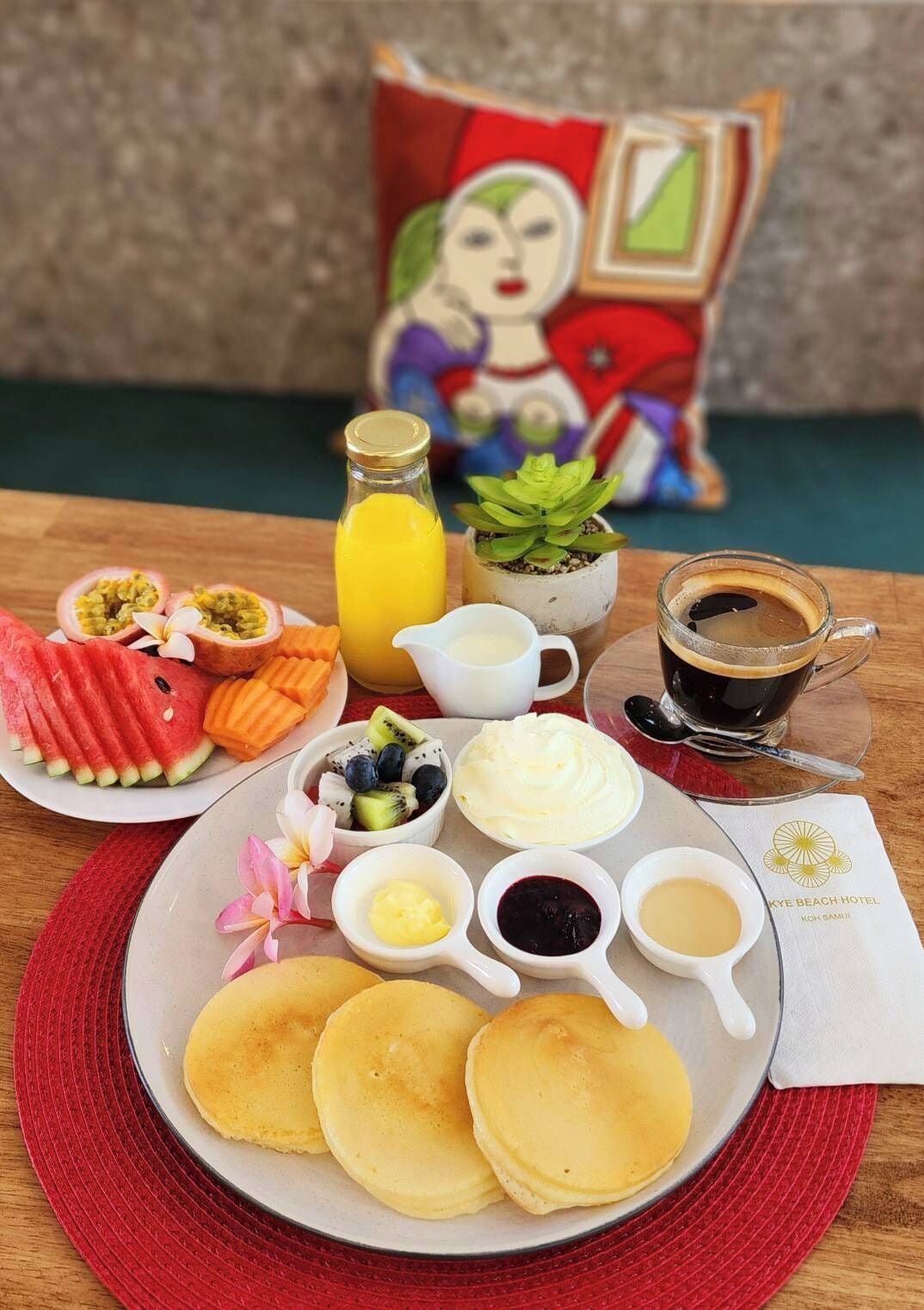 A breakfast spread with pancakes, fruit, and beverages on a wooden table.