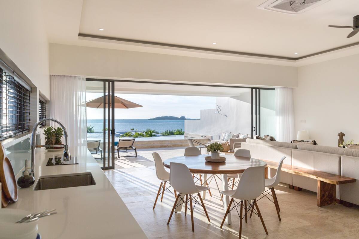 A modern kitchen with a large dining table and chairs, a built-in oven, and a view of the ocean.
