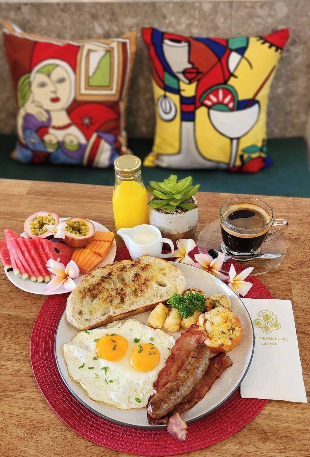 Ein Frühstücksteller mit Eiern, Speck, Würstchen, Rösti und einem Glas Orangensaft.