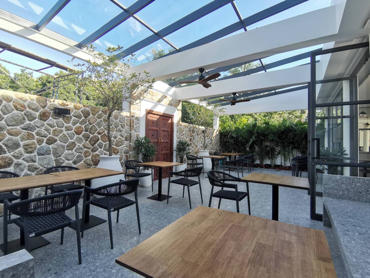 Ein Terrassenbereich im Freien mit Steinmauern, Holztischen und schwarzen Stühlen.
