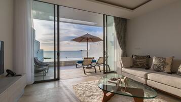 A modern living room with a glass coffee table, a sofa, and a view of the sea through large sliding glass doors.