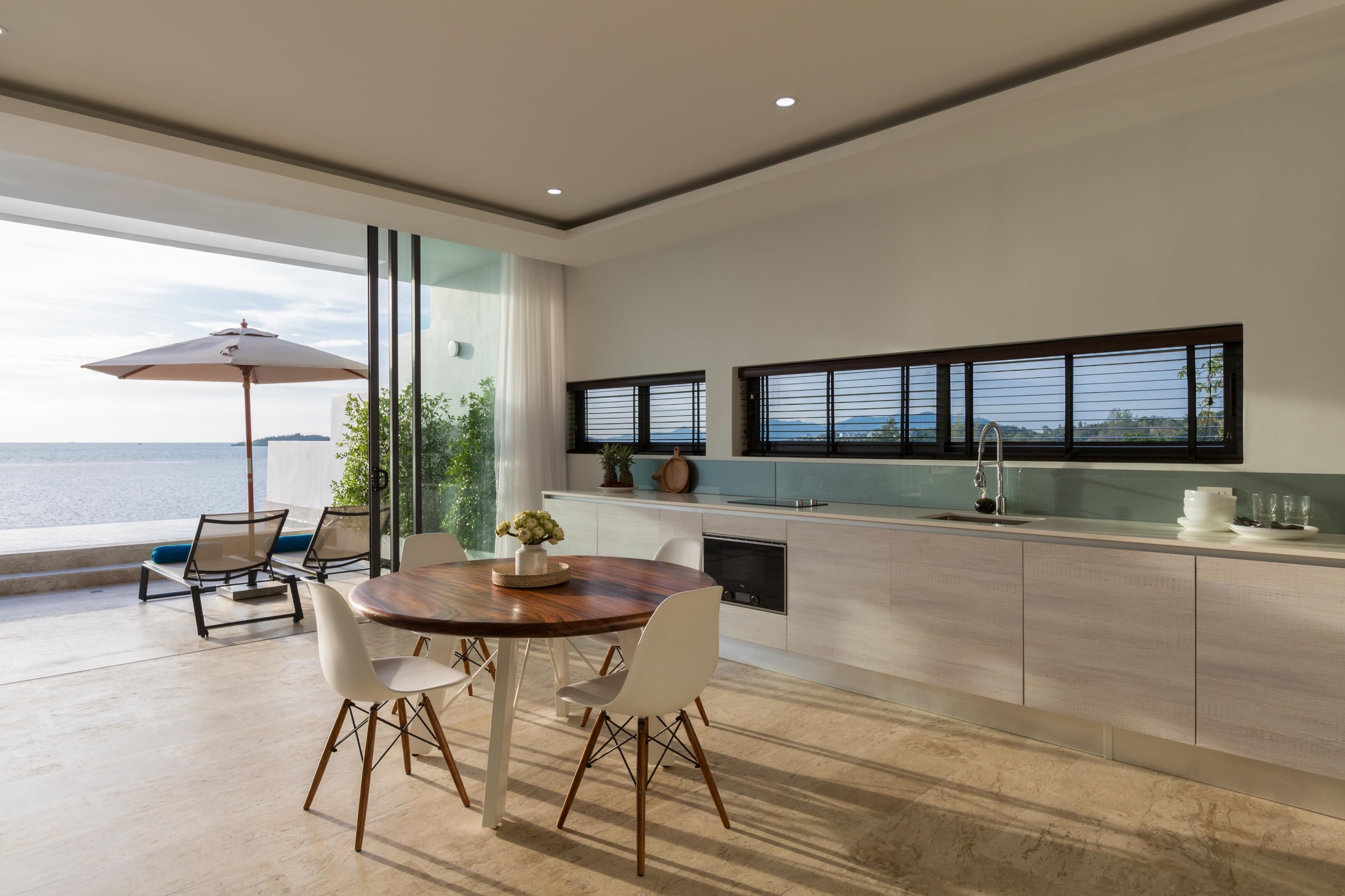 Una cocina moderna con una isla grande, comedor con sillas y vista al mar.