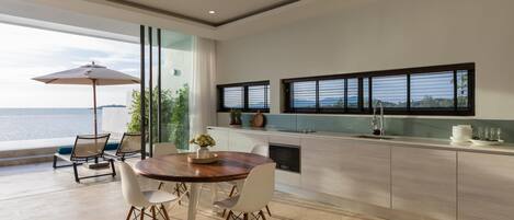 Una cocina moderna con una isla grande, comedor con sillas y vista al mar.