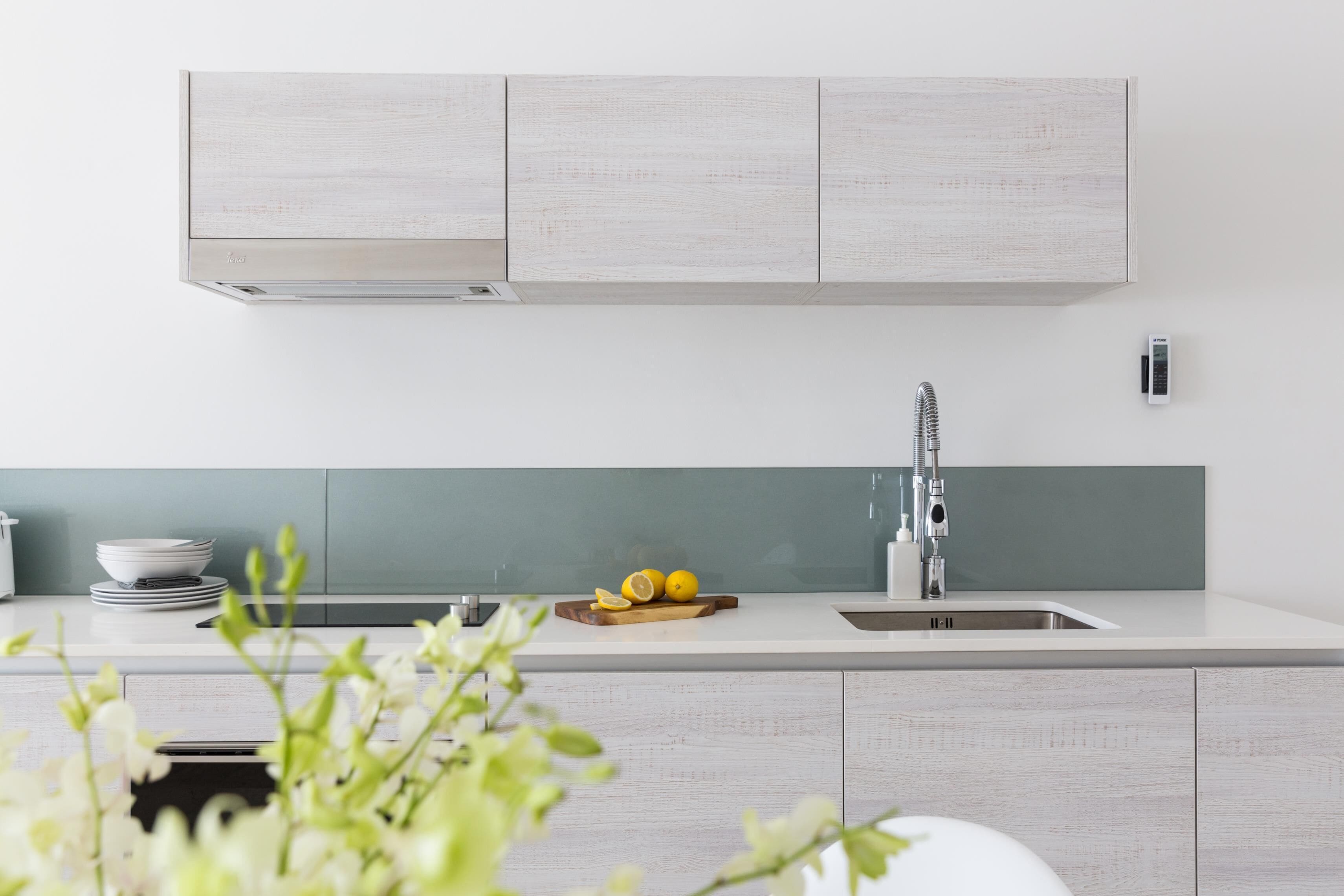Une cuisine moderne avec un plan de travail blanc, un évier en acier inoxydable et un pare-feu vert.
