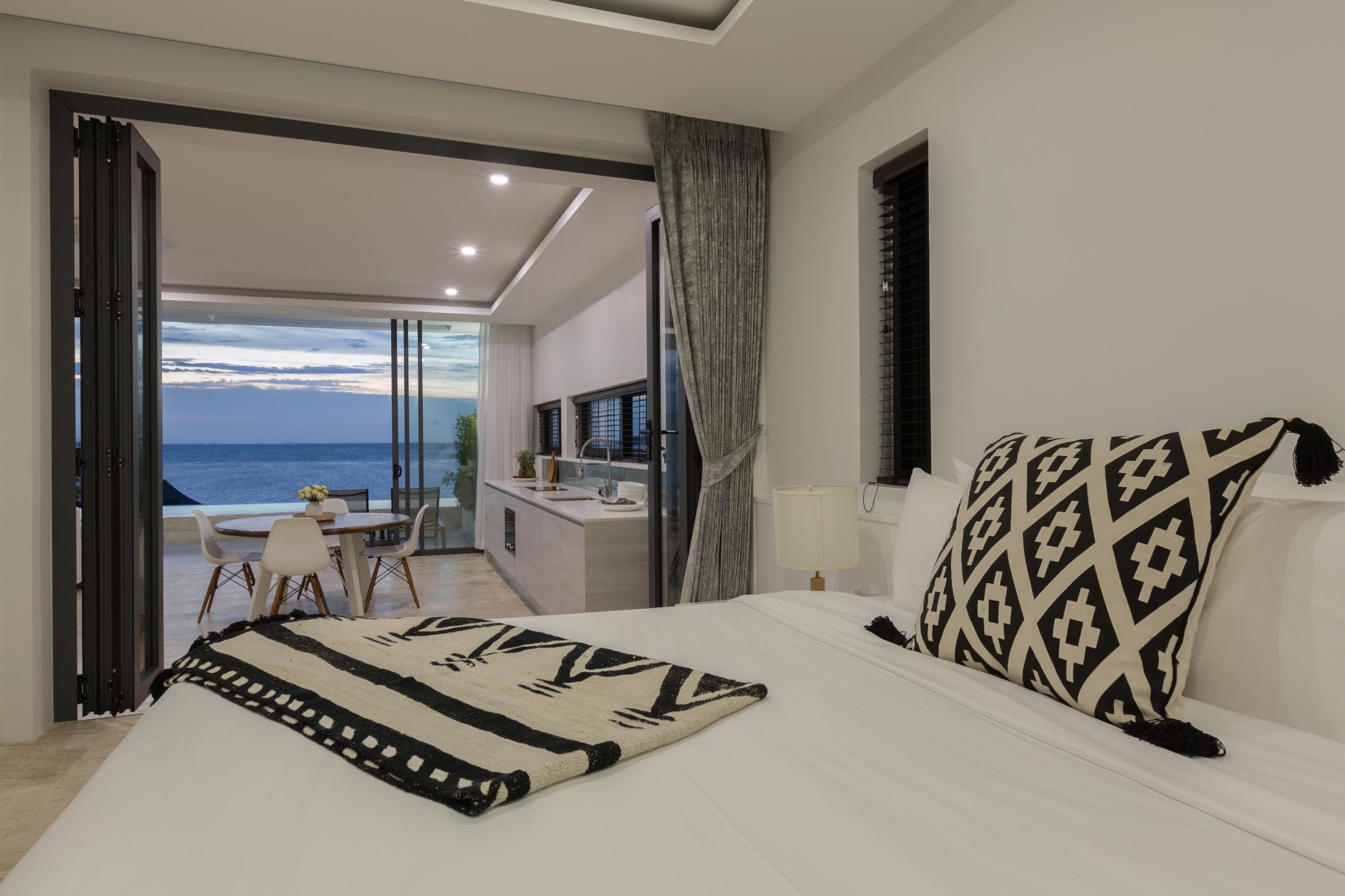 Un dormitorio con una cama grande, vistas al mar, un balcón con zona de comedor y un baño moderno.