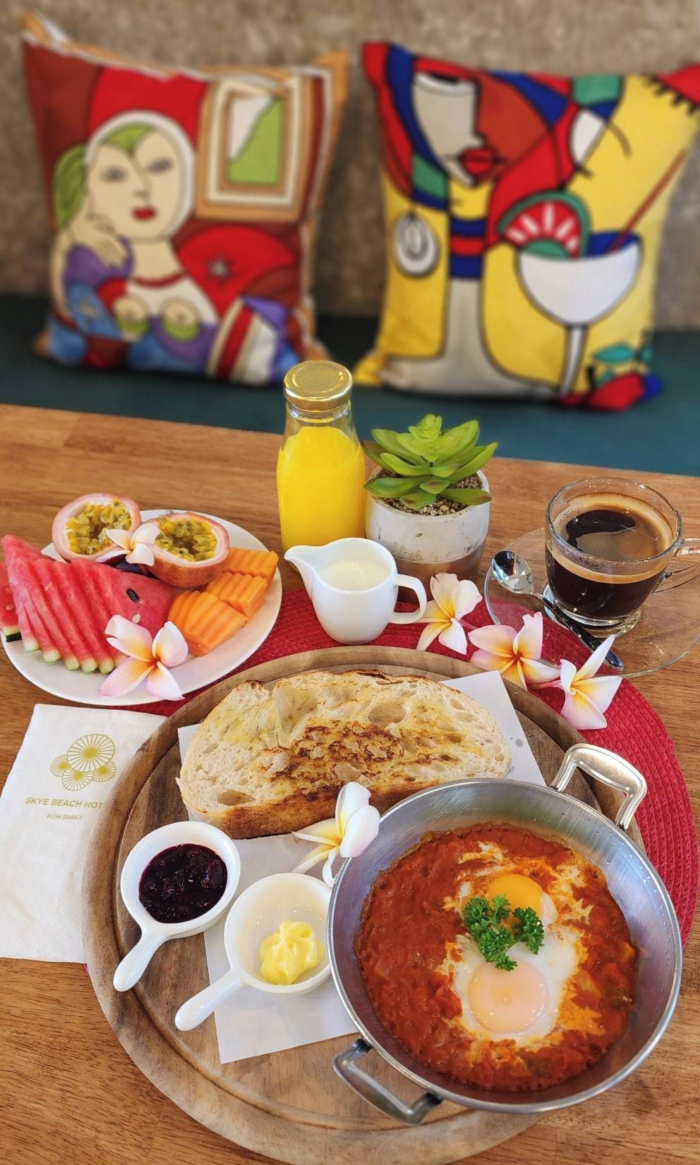 Un assortiment de plats pour le petit-déjeuner, comprenant des œufs, du pain et des fruits, disposés sur un plateau en bois.