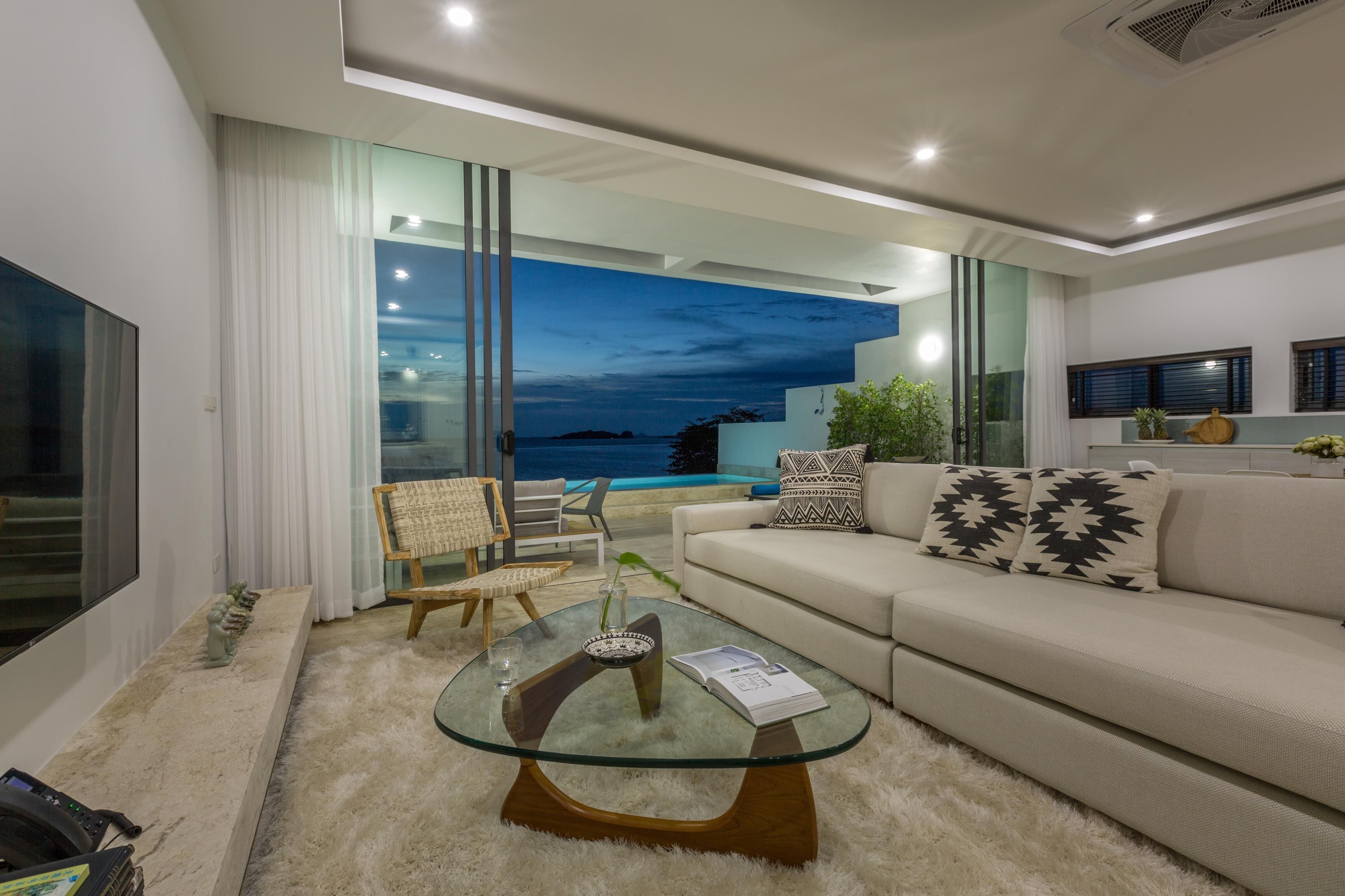 A modern living room with a glass coffee table, a sofa, and a view of the ocean.
