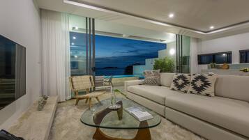 A modern living room with a glass coffee table, a sofa, and a view of the ocean.
