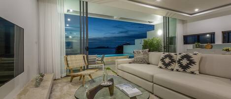 A modern living room with a glass coffee table, a sofa, and a view of the ocean.