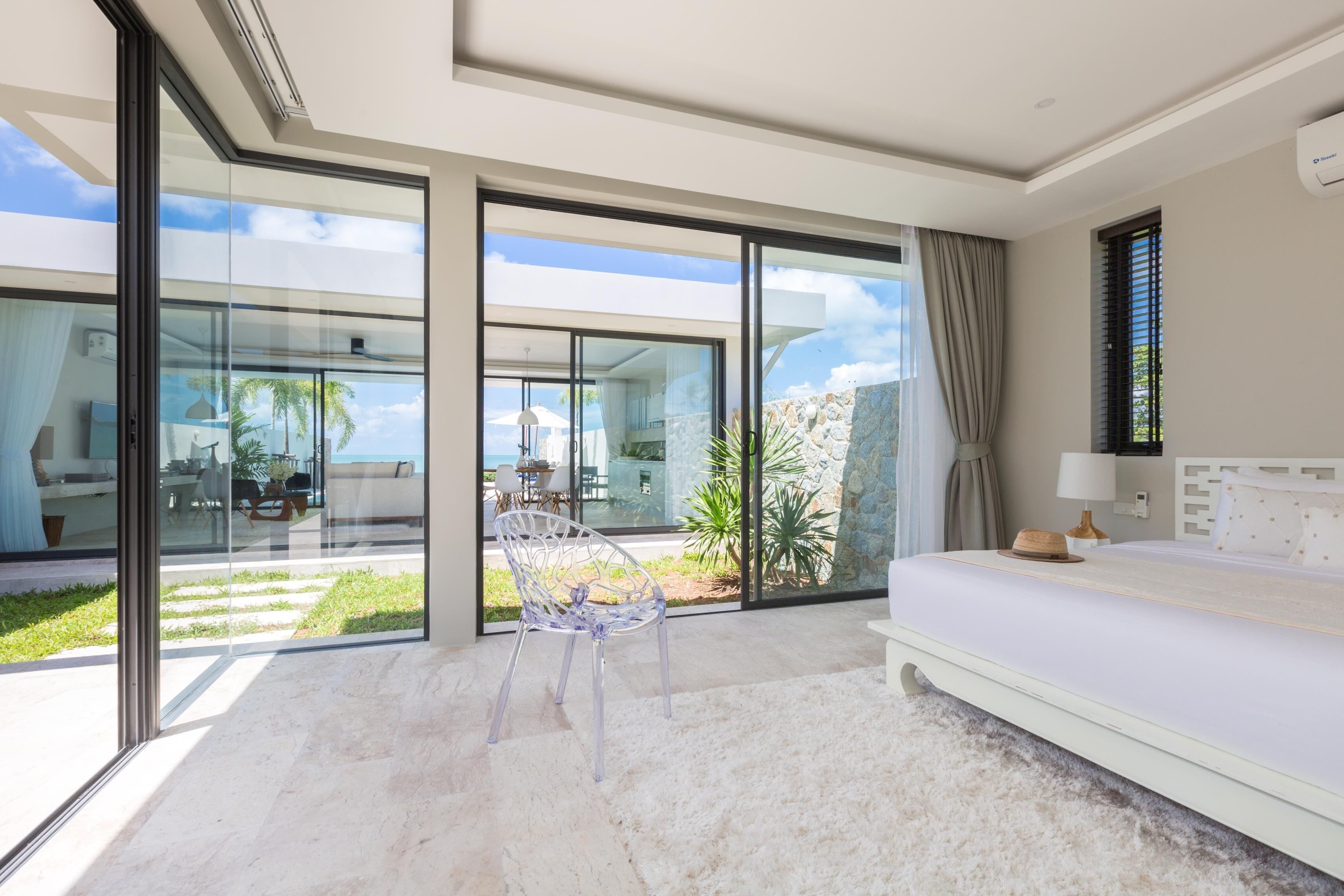 Un dormitorio moderno con un gran ventanal que da a un balcón, una cama blanca y vistas despejadas del exterior.