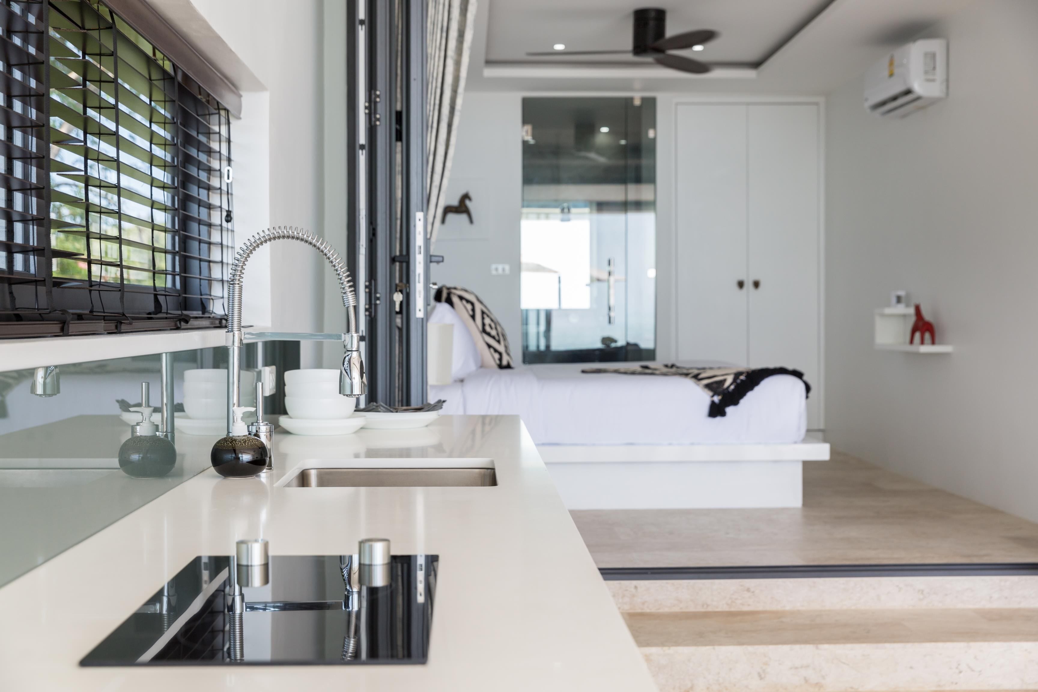 A modern kitchen with a sleek countertop, a built-in sink, and a window with blinds.