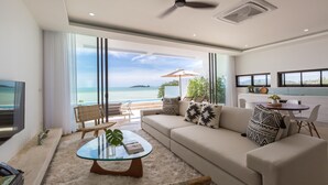 Una sala de estar moderna con una mesa de centro de vidrio, sofá color beige y vista al mar.