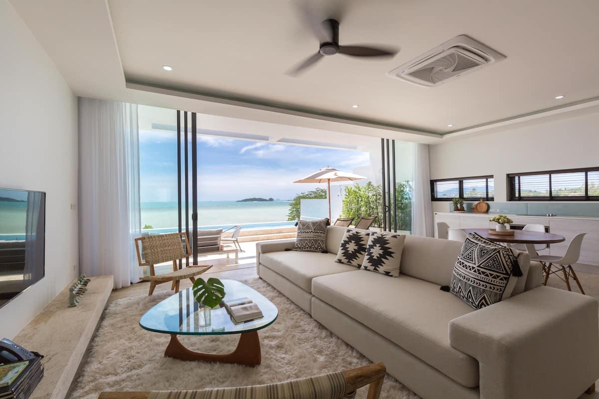 A modern living room with a glass coffee table, beige sofa, and a view of the sea.