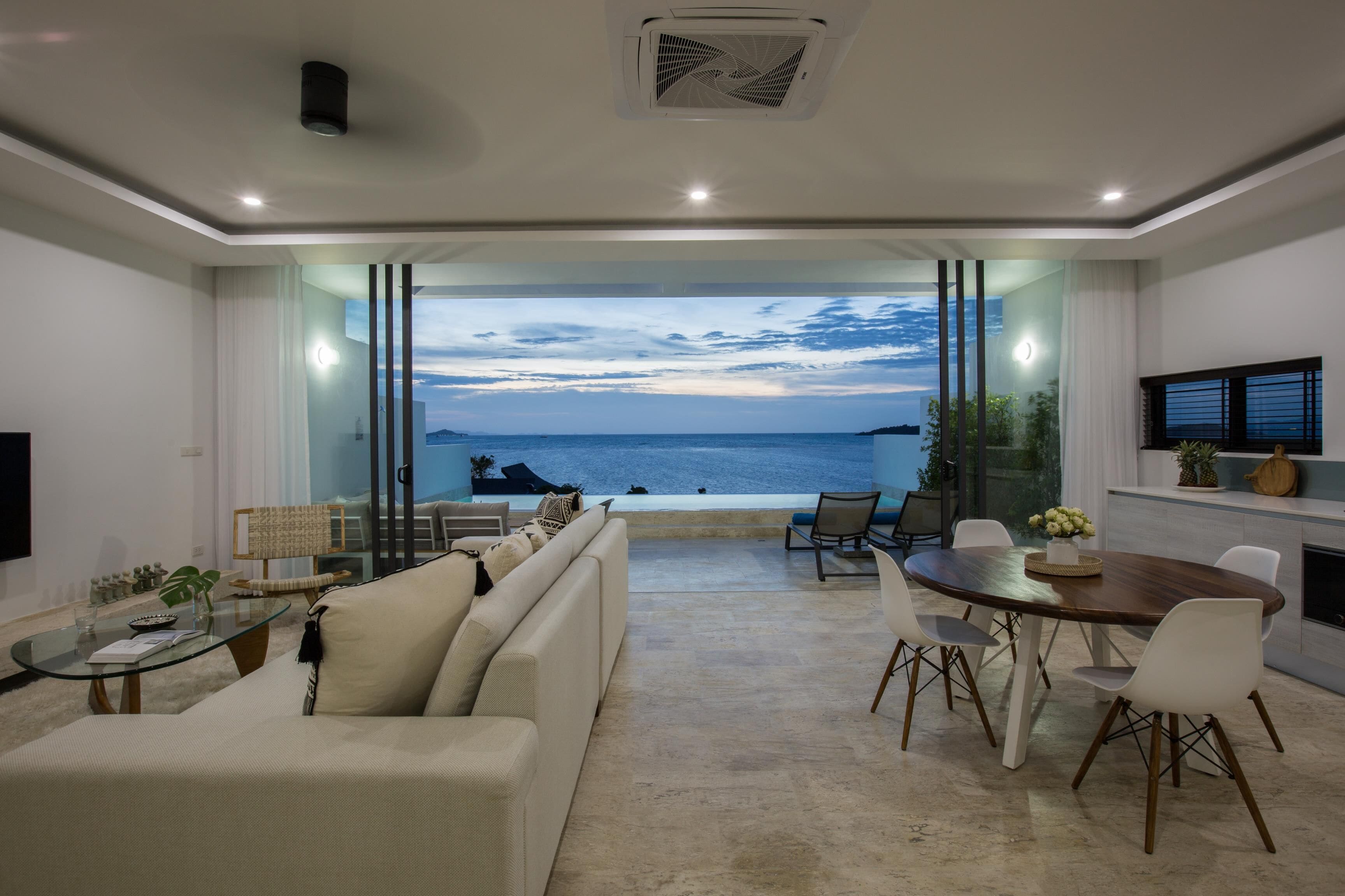 A modern living room with a large glass wall offering a view of the sea.