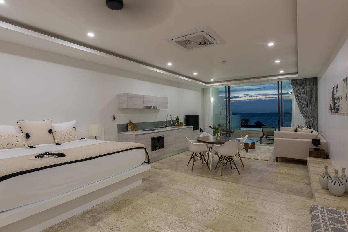 A modern bedroom with a large bed, a dining area, and a view of the ocean.
