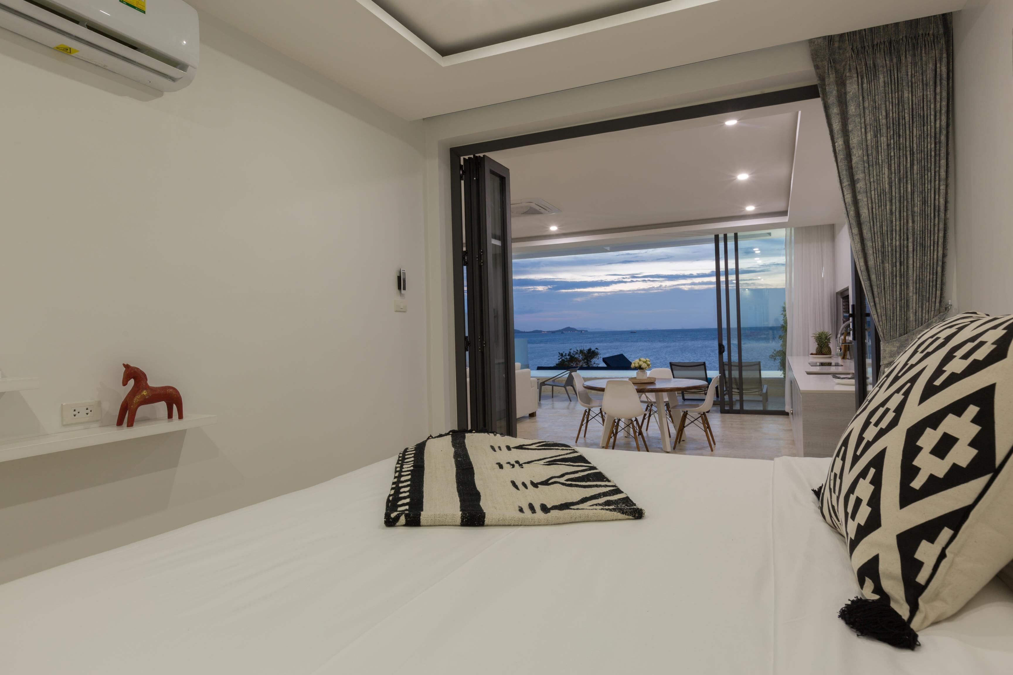 A modern bedroom with a large bed, a view of the sea, and a dining area with a table and chairs.