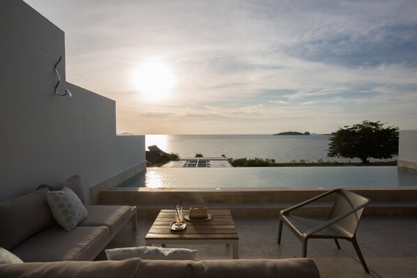 A balcony with a view of the sea, a sofa, a table with a hat and glass, and a chair. - Skye Beach Hotel (Koh Samui)
