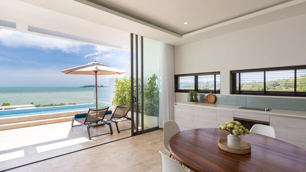 Una cocina moderna con vistas al mar, un comedor con mesa de madera y un área de estar con puerta de vidrio que da al océano.