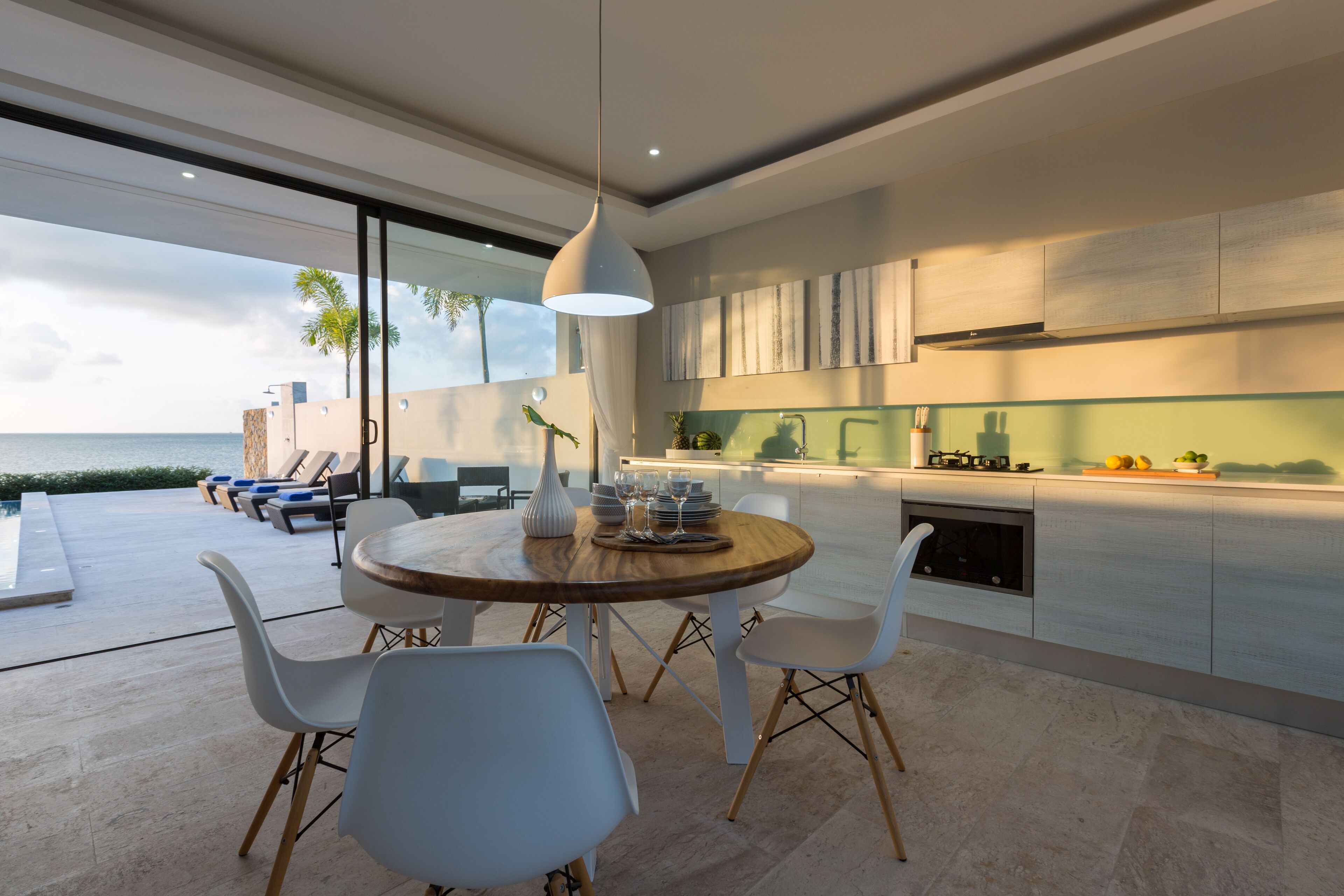 A modern kitchen with a large island, white chairs, and a view of the ocean.
