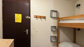 Une petite pièce, de taille modeste, comprenant un lit superposé, un bureau en bois et une porte sur laquelle est affiché un avis.