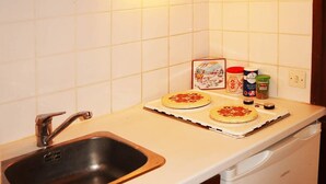 Une cuisine équipée d’un évier, d’un four à micro-ondes et d’un plan de travail sur lequel se trouvent deux fonds de pizza et divers ingrédients pour les garnir.