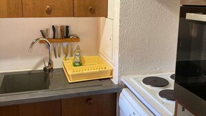 Una cocina con armarios de madera, un lavamanos de acero inoxidable, un escurreplatos amarillo y una estufa.