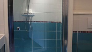Une douche dotée d’une porte en verre, d’un pommeau de douche à main et d’un panneau de commande fixé au mur.