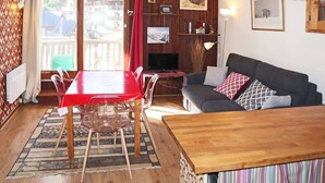 A cozy living room with a wooden dining table, clear chairs, a sofa with patterned cushions, and a TV. - 2-room apartment for 6 people above the mall, Les Orres (Les Orres)