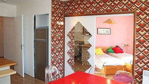 A compact room with a kitchenette, a dining area with a red table, and a bed with colorful pillows. - 2-room apartment for 6 people above the mall, Les Orres (Les Orres)
