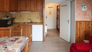A compact kitchen with wooden cabinets, a small refrigerator, and a tiled backsplash.