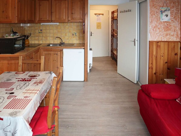 Cozinha compacta com armários de madeira, uma pequena geladeira e painel de azulejos.