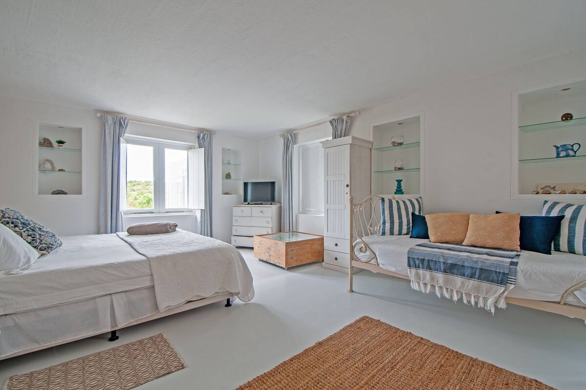 A bedroom with two beds, a TV, a wardrobe, and a window with curtains.