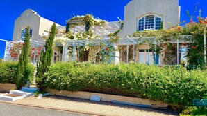 A two-story building with a white facade, large windows, and a white picket fence. - Charlotte House (Still Bay)