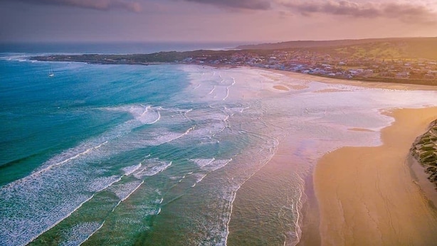 An aerial view of a coastal area with a beach, ocean, and distant land with buildings. - Charlotte House (Still Bay)