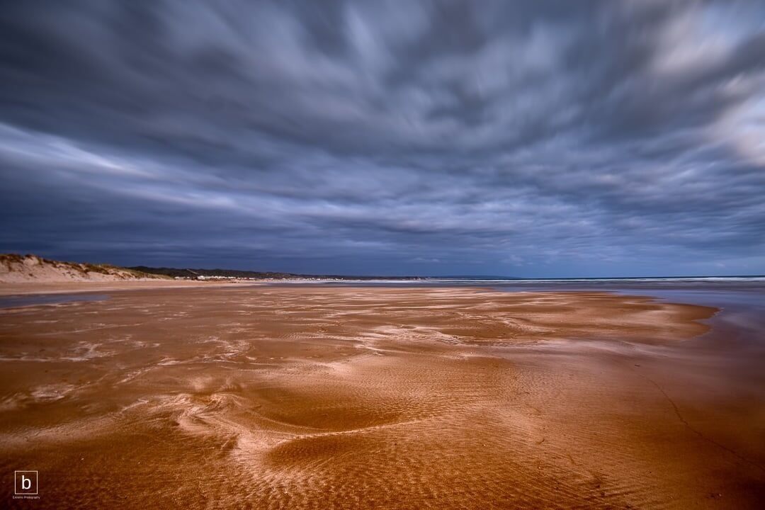 A beach with a wide expanse of sand and a cloudy sky.