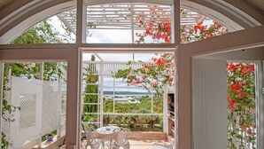 A covered patio with a table and chairs, a white fence, and a view of greenery and buildings. - Charlotte House (Still Bay)