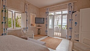 A bedroom with a large bed, a TV, and a balcony with curtains. - Charlotte House (Still Bay)
