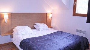 A bedroom with a wooden headboard, two bedside lamps, a bed with white and dark blue bedding, and a window with a view of trees. - Superb 10 pax duplex with pool and jacuzzi in Les Orres 1800 (Les Orres)
