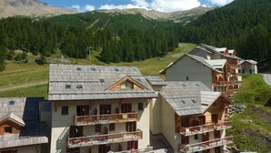A mountain resort with chalet-style buildings, balconies, and a view of forested mountains. - Superb 10 pax duplex with pool and jacuzzi in Les Orres 1800 (Les Orres)