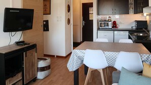 A compact living space with a TV, kitchenette, dining area, and a sliding door. - Renovated apt with pool, sauna, hammam and wifi at Les Orres 1800 (Les Orres)