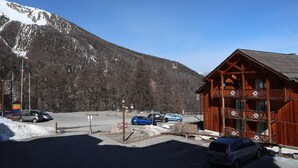 A wooden lodge with a balcony, a parking lot, and a mountain backdrop. - Renovated apt with pool, sauna, hammam and wifi at Les Orres 1800 (Les Orres)